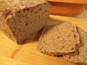 Ein Kastenbrot in Nahaufnahme, wovon 2 Scheiben abgeschnitten davor liegen. Das Brot liegt auf einem Holzbrett. Das Bild ist das Leitbild für den Beitrag: "Sauerteigbrot selber backen"